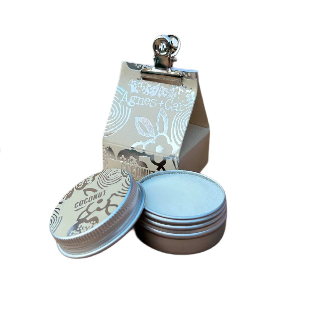 Bálsamo labial natural de coco Agnes + Cat en envase metálico con caja artesanal, fórmula vegana con manteca de karité y aceites nutritivos, hidratación profunda y aroma tropical.