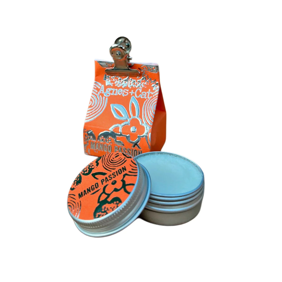 Bálsamo labial natural Mango y Fruta de la Pasión de Agnes + Cat en envase metálico con diseño naranja vibrante, fórmula vegana y aroma exótico tropical
