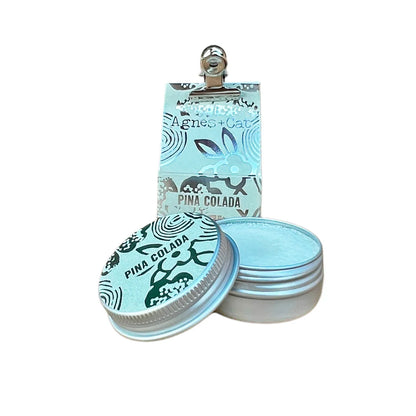 Bálsamo labial natural de Piña Colada en envase metálico con packaging decorativo de Agnes + Cat, hidratante vegano con aroma tropical y fórmula con manteca de karité, mango y aguacate.