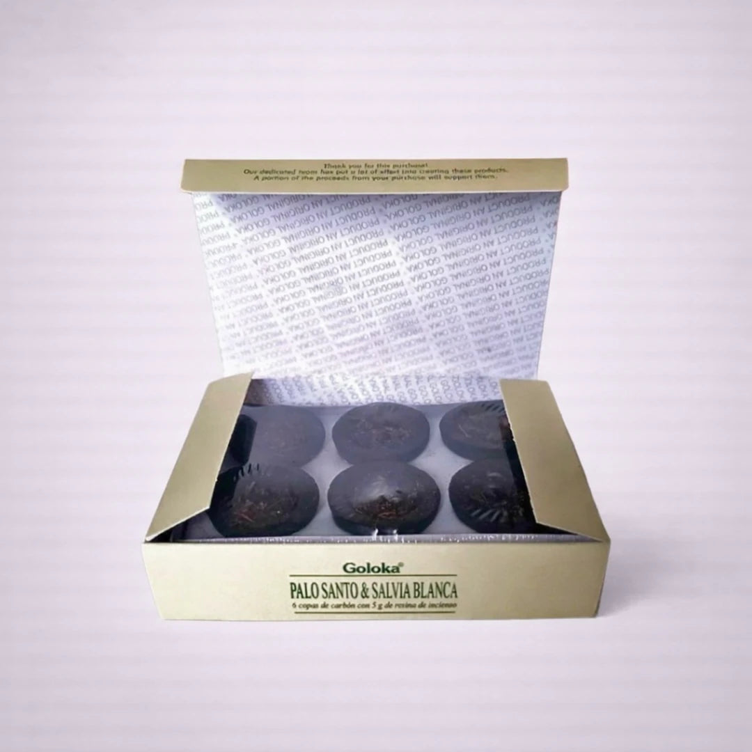 Caja abierta de copas de incienso Goloka Palo Santo y Salvia Blanca con carbones de resina sobre fondo gris suave