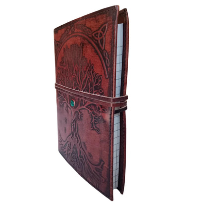 Vista lateral del cuaderno de cuero con diseño del Árbol de la Vida y papel rayado en el interior, con correa envolvente y piedra natural.