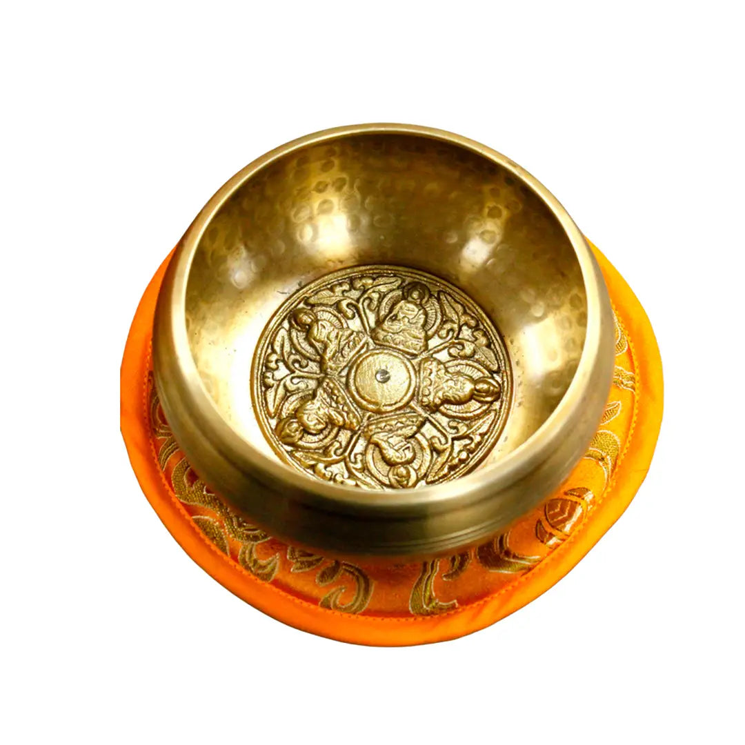 Cuenco tibetano artesanal con grabado de 5 budas en su interior, sobre cojín decorativo naranja.