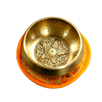 Cuenco tibetano artesanal con grabado de 5 budas en su interior, sobre cojín decorativo naranja.