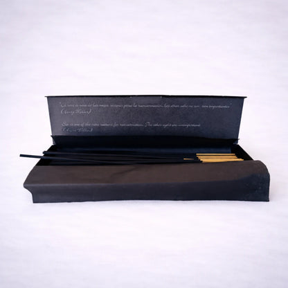 Caja abierta de incienso de canela con varillas artesanales negras y punta dorada sobre fondo gris suave