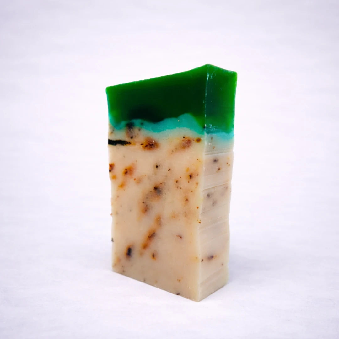 Jabón artesanal de té verde natural con capas verdes y base exfoliante sobre fondo gris suave