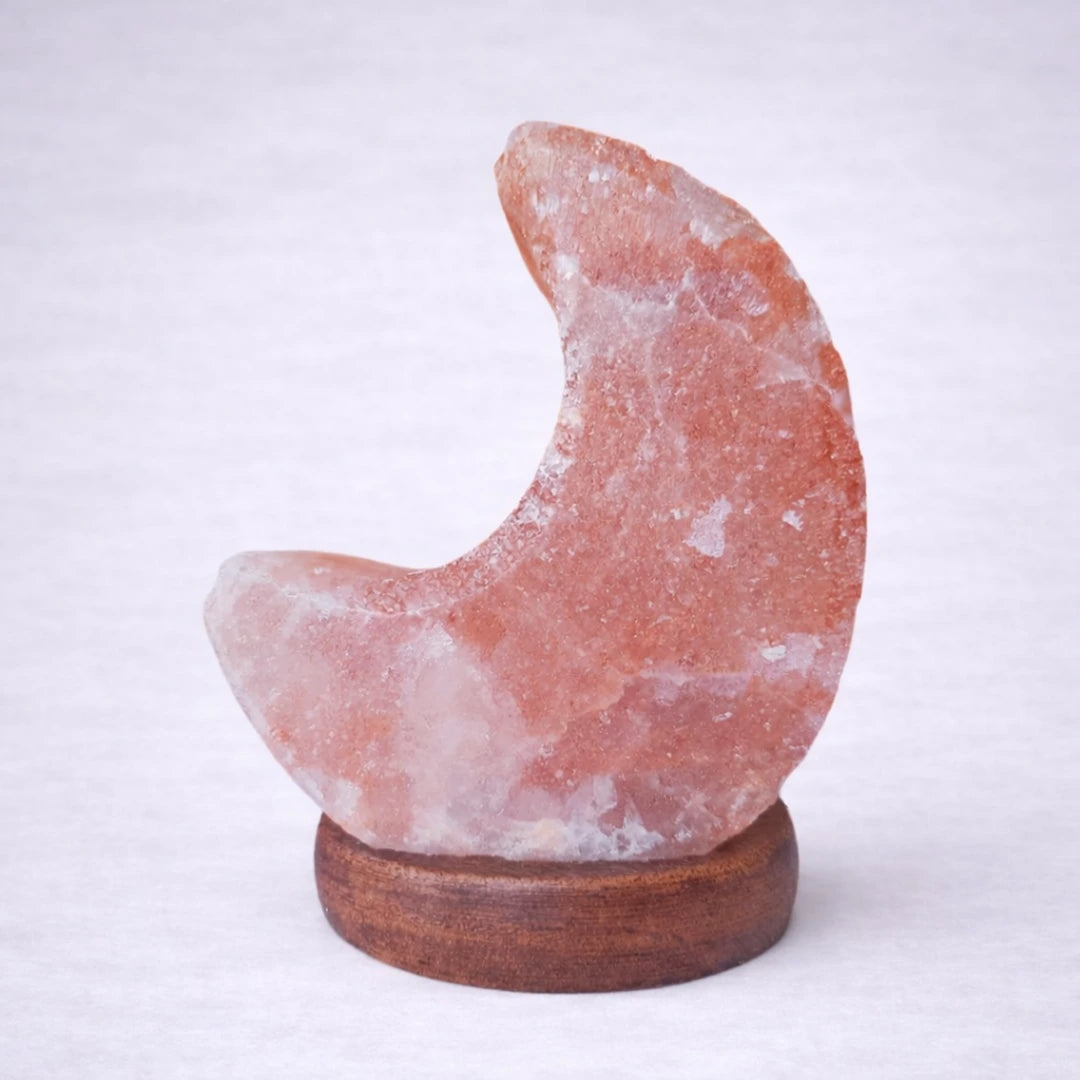 Lámpara de sal del Himalaya en forma de luna sobre base de madera con fondo grisáceo suave