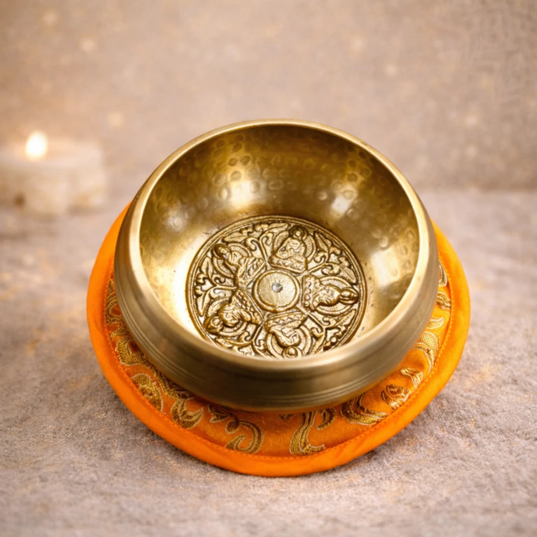 Cuenco tibetano artesanal con tapete acolchado y decorativo, producto de gran calidad con grabado de los 5 budas, en un fondo cálido espiritual