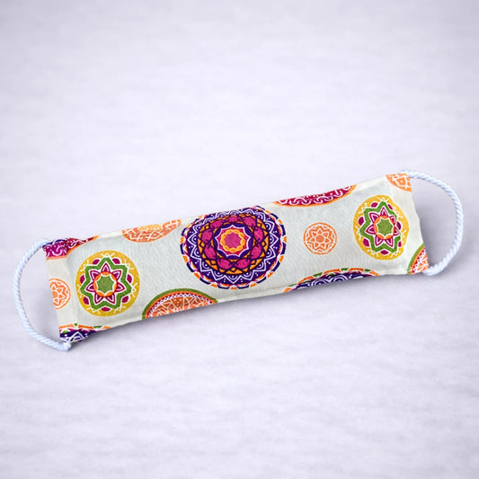 Saco térmico natural con estampado de mandalas multicolor, ideal para relajación y alivio muscular, presentado sobre fondo gris suave.