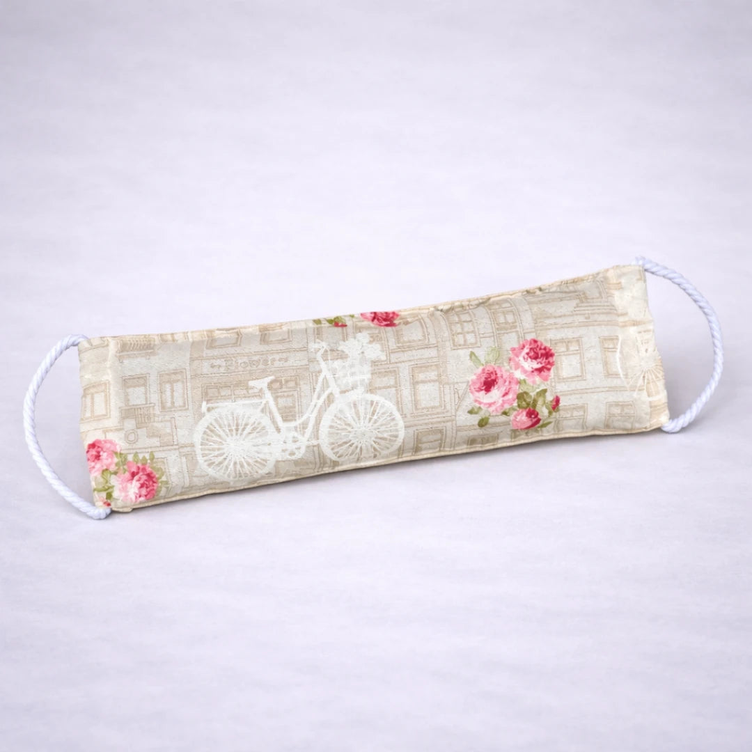 Saco térmico artesanal con estampado vintage de bicicleta y rosas, pensado para calor terapéutico y bienestar, sobre fondo gris suave.