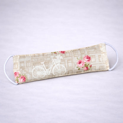 Saco térmico artesanal con estampado vintage de bicicleta y rosas, pensado para calor terapéutico y bienestar, sobre fondo gris suave.