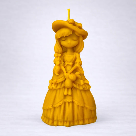 Vela artesanal de cera de abeja con figura femenina elegante y sombrero, conocida como dama del tiempo, sobre fondo gris suave y estilo minimalista.