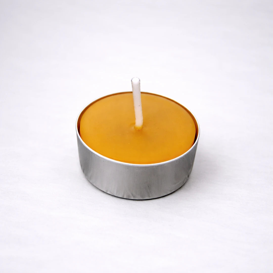 Vela de té de cera de abeja natural en cápsula de aluminio sobre fondo gris suave