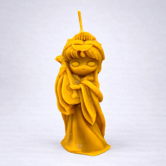 Vela artesanal de cera de abeja con figura femenina oriental sosteniendo un instrumento musical, sobre fondo gris suave y neutro