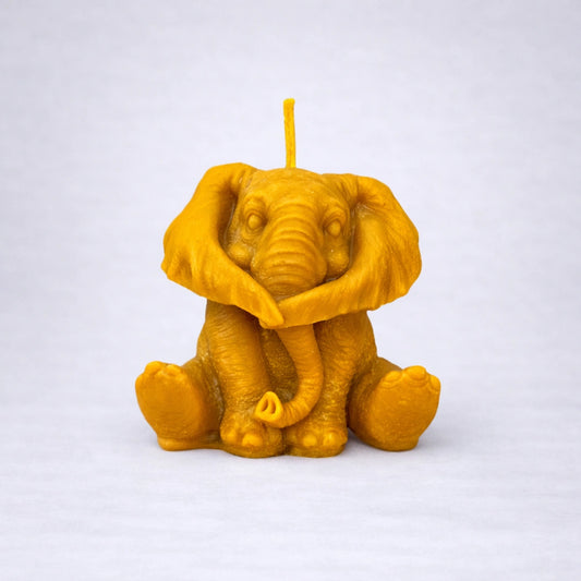 Vela artesanal de cera de abeja en forma de elefante con las orejas cubriendo el rostro, simbolizando la escucha interior y la calma, sobre fondo gris suave.