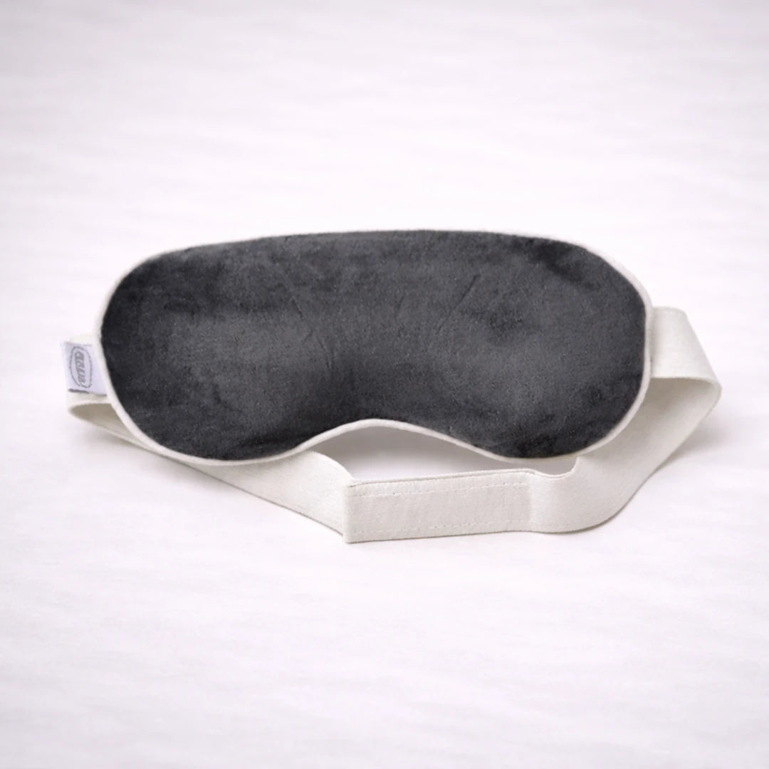 Antifaz de descanso negro suave con cinta elástica blanca sobre fondo neutro, ideal para relajación y sueño profundo