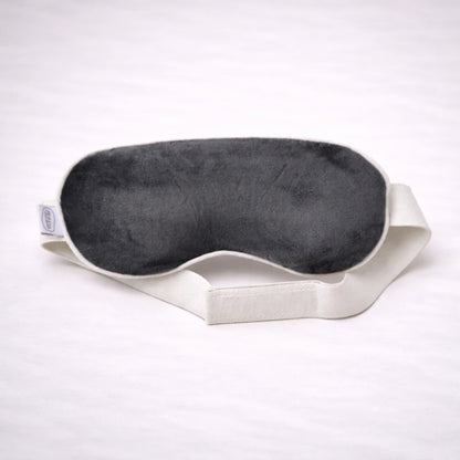 Antifaz de descanso negro suave con cinta elástica blanca sobre fondo neutro, ideal para relajación y sueño profundo