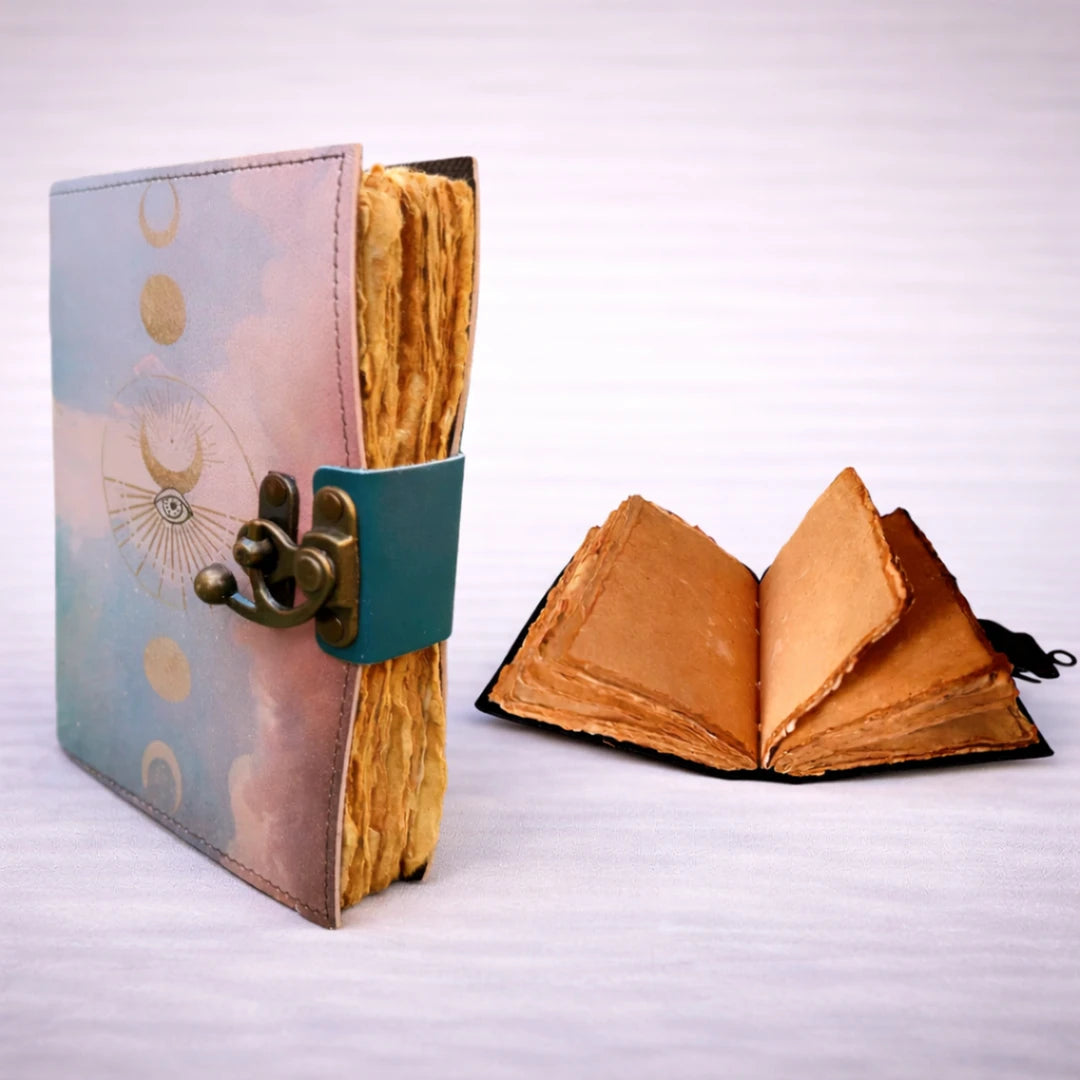 Cuaderno artesanal de cuero con cierre metálico, vista lateral mostrando páginas de papel rústico hechas a mano y cuaderno abierto en segundo plano.