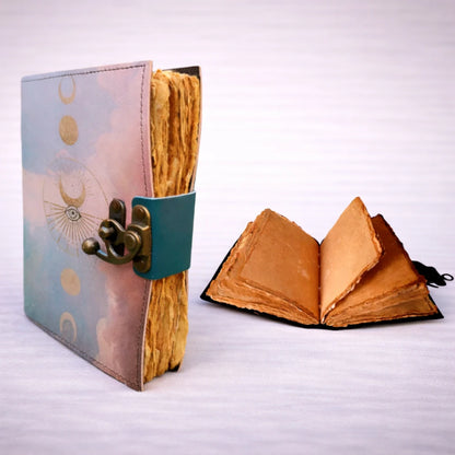 Cuaderno artesanal de cuero con cierre metálico, vista lateral mostrando páginas de papel rústico hechas a mano y cuaderno abierto en segundo plano.