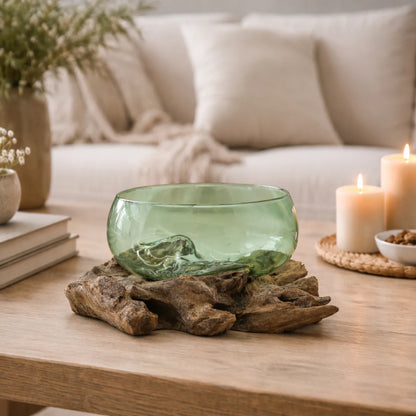 Cuenco de vidrio verde sobre base de madera natural en mesa de salón con velas