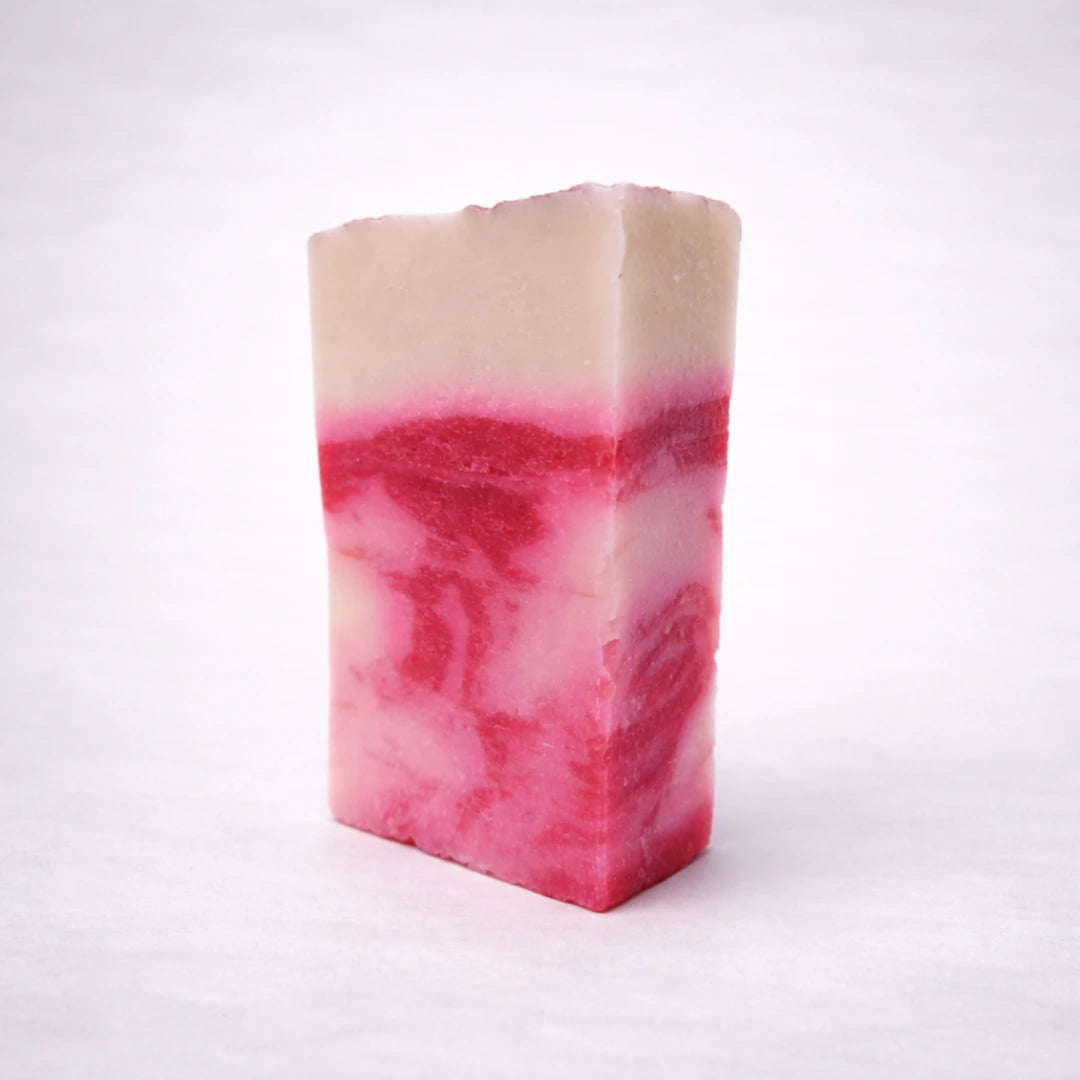 Jabón artesanal de arcilla roja hecho a mano, con vetas rosadas y blancas, sobre fondo gris suave neutro