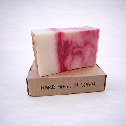Jabón artesanal de arcilla roja sobre caja kraft, elaborado a mano en España, con acabado natural y fondo gris suave