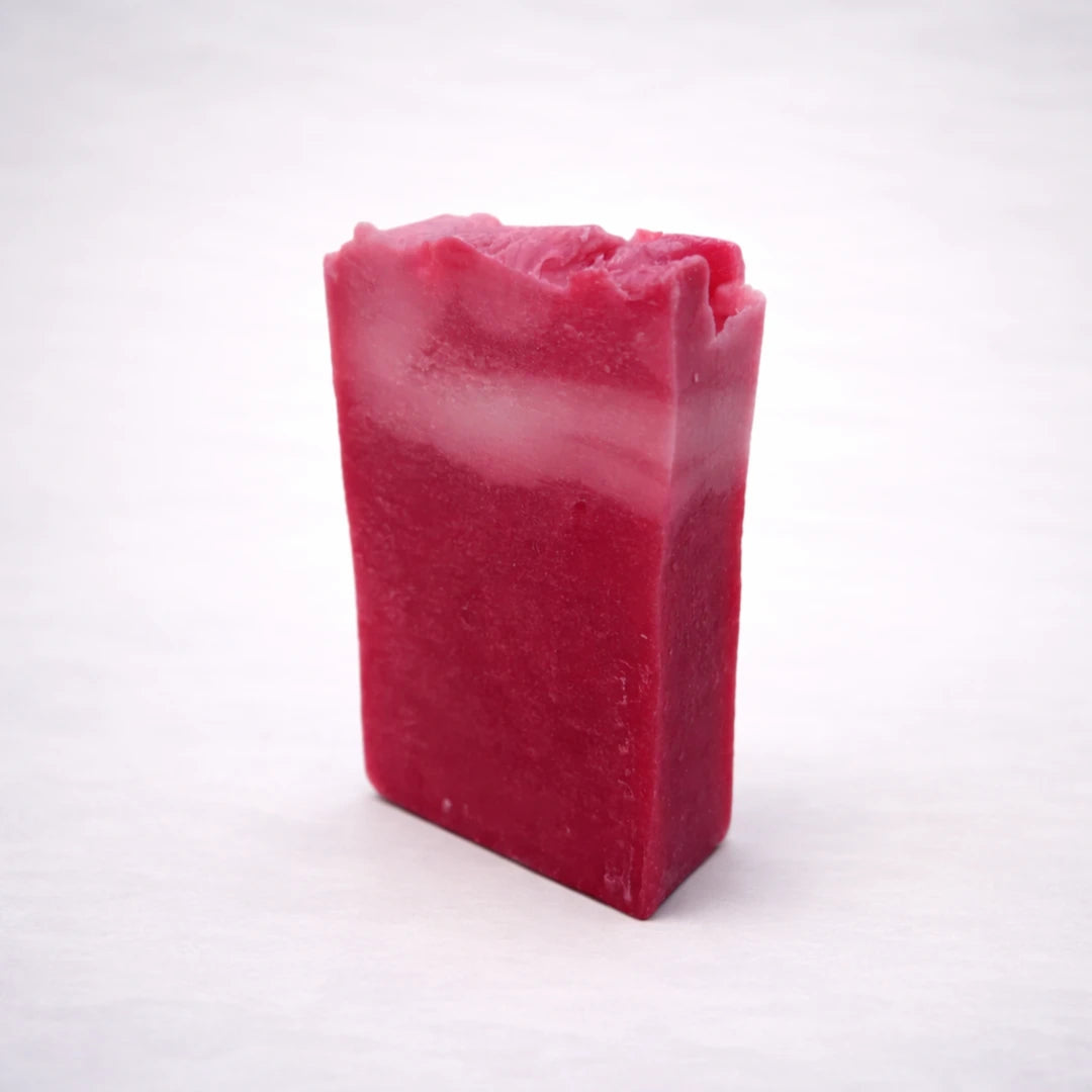 Jabón artesanal de karité rosa hecho a mano en España, pastilla natural hidratante con acabado rústico sobre fondo gris claro