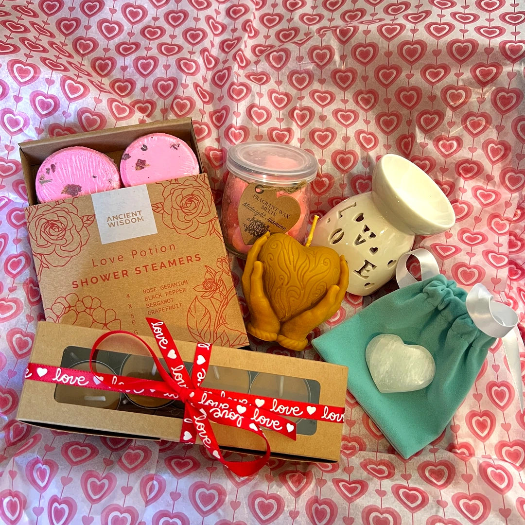 Pack Amor en Calma con vaporizador cerámico con luz, ceras aromáticas en forma de corazón, velas artesanales y accesorios de bienestar sobre fondo romántico
