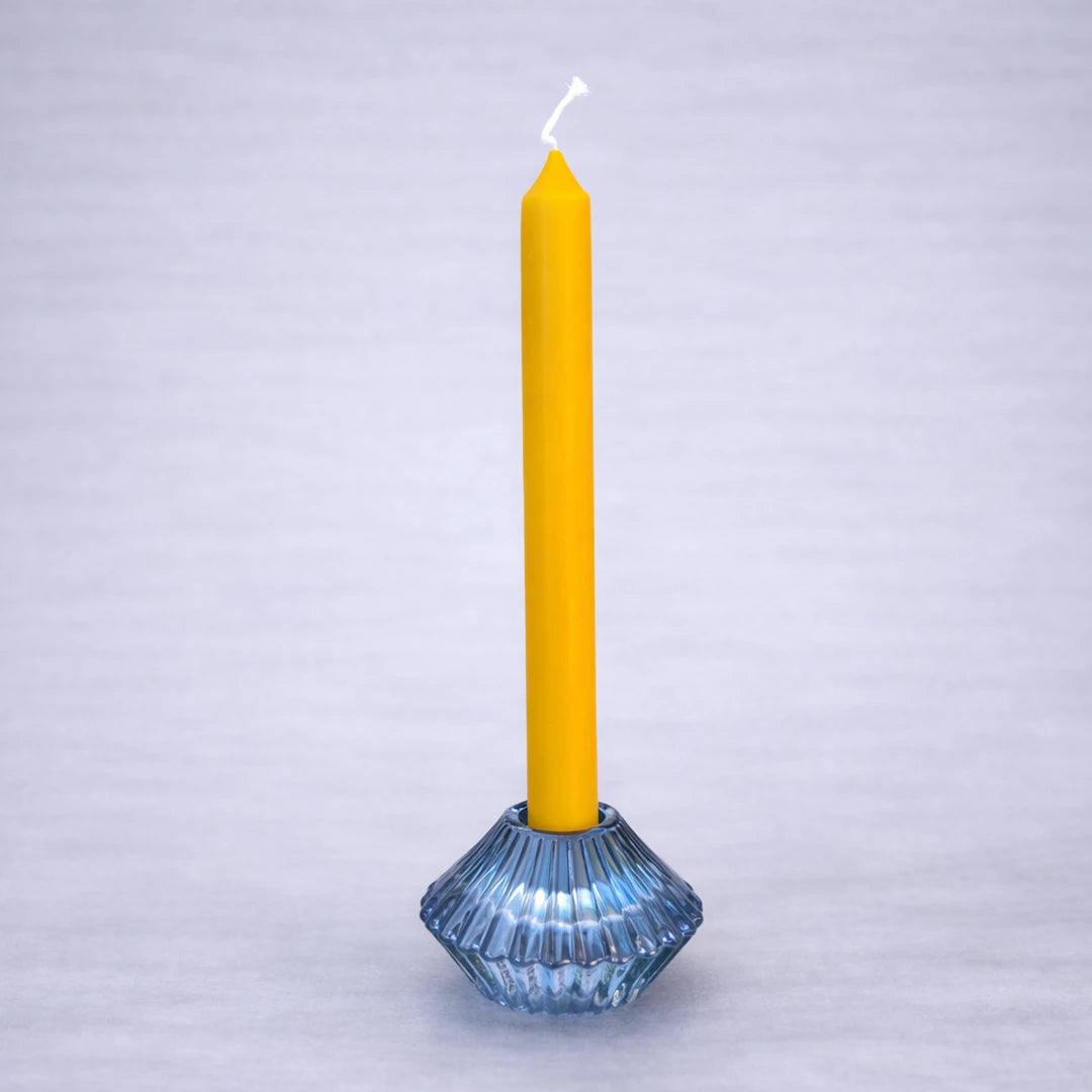 Portavelas reversible de cristal azul con vela larga de miel sobre fondo gris suave