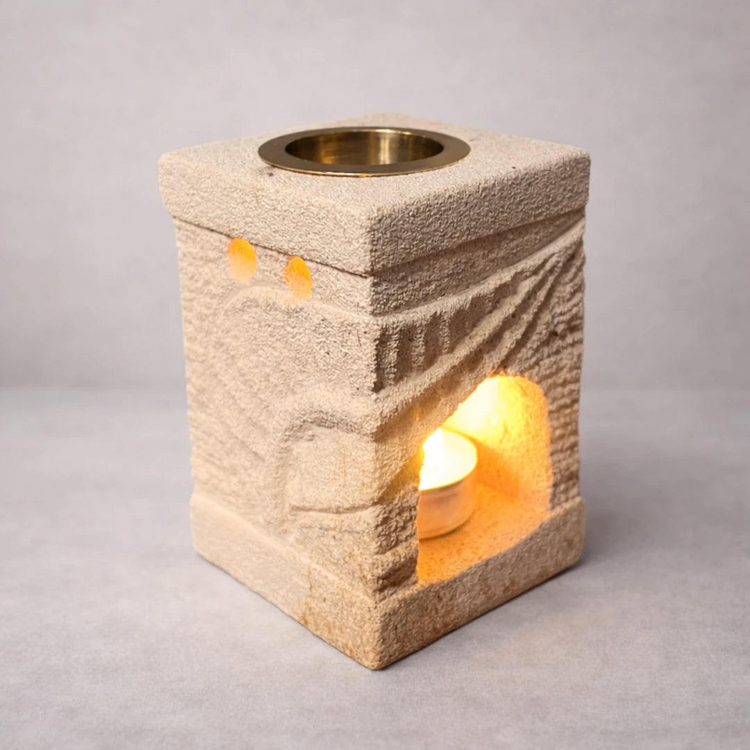 Quemador de aceites Java de piedra tallada con cuenco de latón y vela encendida creando luz cálida