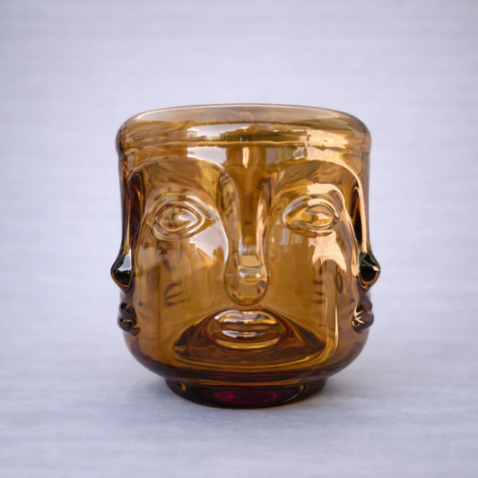 Portavelas de cristal ámbar con diseño elegante de rostro buda y acabado brillante sobre fondo neutro