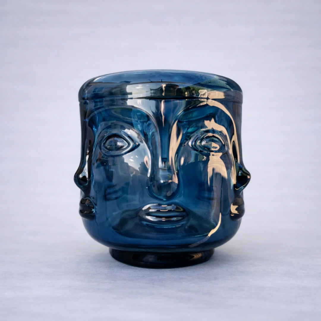 Portavelas de cristal azul con diseño elegante de rostro buda sobre fondo gris claro y sombra natural