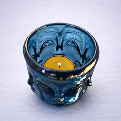 Portavelas buda de cristal azul con vela de té en el interior sobre fondo gris suave